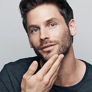 Mann berührt seinen frisch rasierten Bartbereich, was die Glätte und das gepflegte Aussehen hervorhebt.