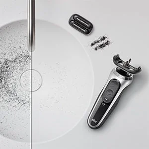 Braun Rasierer Serie 7 neben einem Waschbecken mit abgenommenem Scherkopf und abgeschnittenen Barthaaren.
