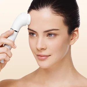 Frau benutzt eine weiße Braun Gesichtsbürste auf ihrer Stirn.