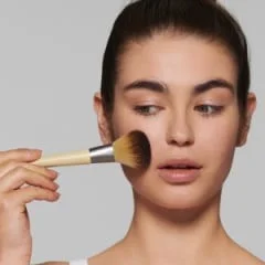 Frau trägt Braun Pinsel auf ihr Gesicht auf, um Make-up aufzutragen.
