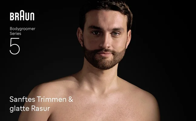 Junger Mann ohne Hemd, der nach der Verwendung des Braun Bodygroomer Series 5 selbstbewusst lächelt.