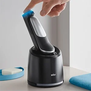 Braun Rasierer in Ladestation, wobei eine Hand den Rasierer berührt.