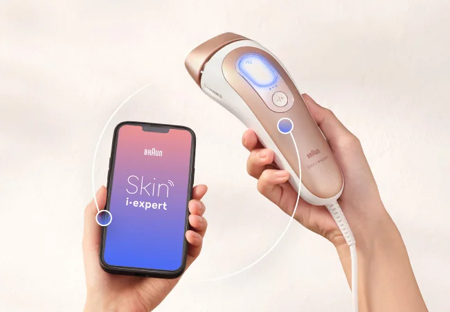 Frau hält Brauns Skin i-expert IPL und ein Smartphone, das sie in Echtzeit per App durch die Anwendung führt.